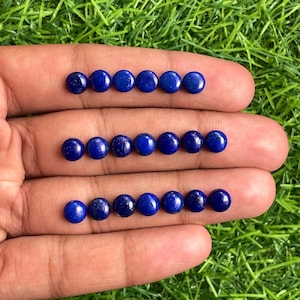 May include: A collection of 18 round, dark blue lapis lazuli cabochons, arranged in three rows of six stones each. The stones are smooth and polished, with a slight shimmer.
