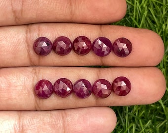 Pode incluir: Oito gemas de rubi facetadas, cada uma com uma cor vermelha profunda, são dispostas em duas filas de quatro em uma mão. As gemas são redondas e têm um acabamento liso e polido.