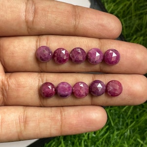 May include: A collection of ten faceted ruby gemstones, each with a unique, irregular shape. The rubies are a deep pink color and have a high polish.