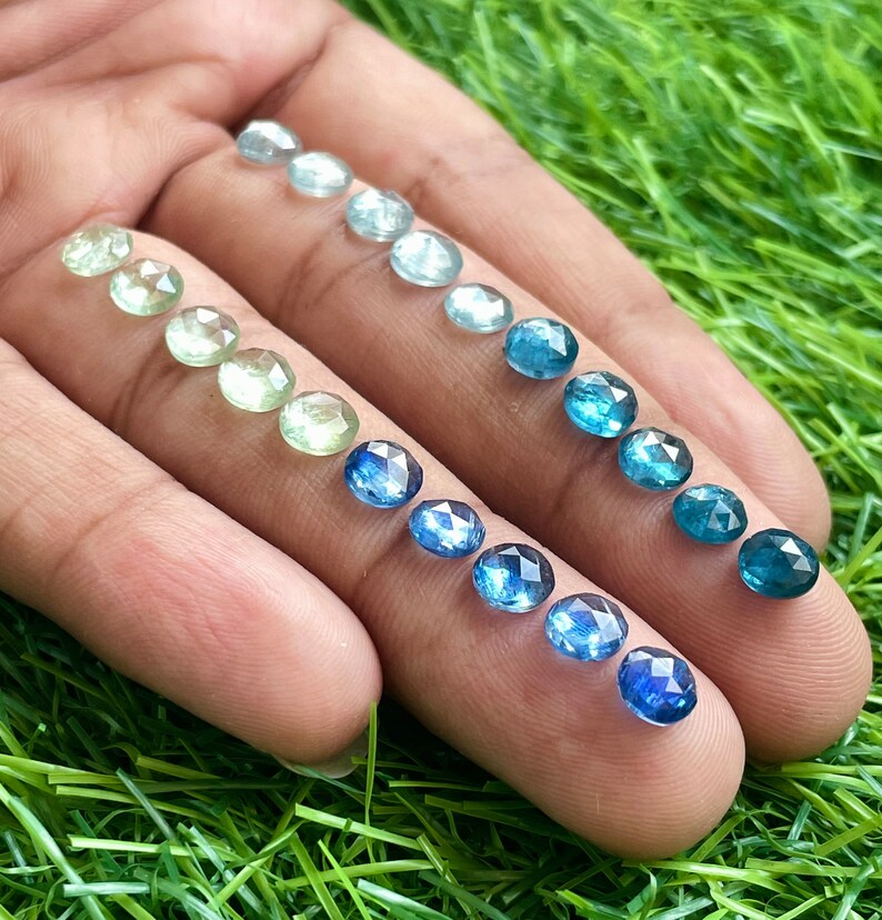 May include: A collection of round, faceted gemstones in various shades of blue and green. The stones are arranged in a gradient from light green to dark blue.
