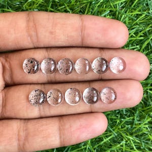 Puede incluir: Diez piedras preciosas redondas, transparentes y en cabujón con inclusiones negras. Las piedras miden aproximadamente 10 mm de diámetro y tienen un acabado liso y pulido.