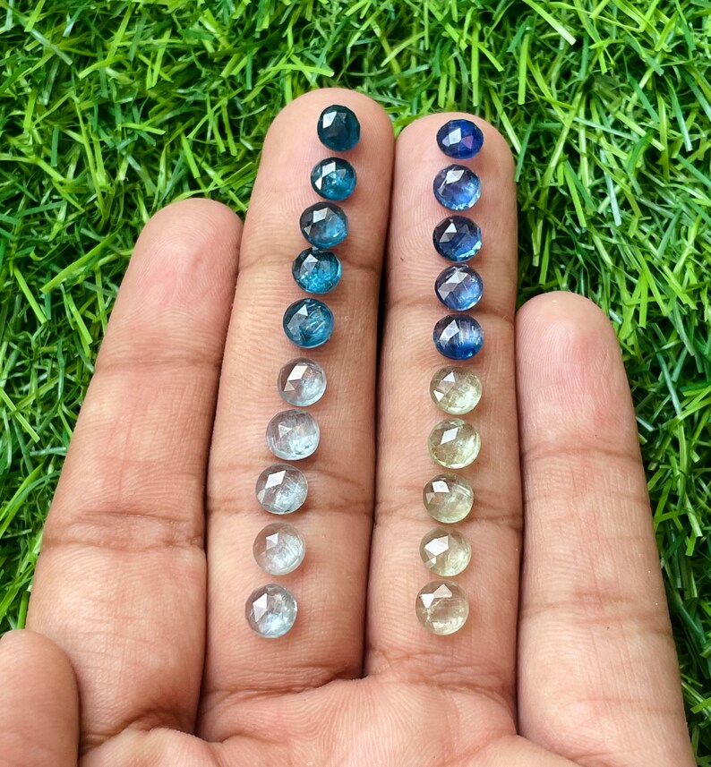 May include: Two rows of faceted gemstones, one row of blue sapphires and one row of green sapphires, arranged in order of color intensity, from dark to light.