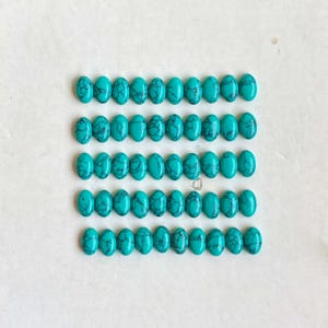May include: A collection of oval turquoise gemstones, each displaying unique dark veining patterns. The polished stones are arranged in rows, highlighting their vibrant blue-green hue. These gemstones are suitable for crafting jewellery.