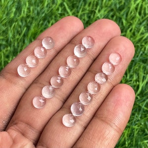 Könnte beinhalten: Eine Sammlung von 14 facettierten, klaren Quarzsteinen, jeder mit einer glatten, abgerundeten Oberfläche. Die Steine sind in zwei Reihen auf einer Hand angeordnet und zeigen ihre transluzente Qualität und zarten Facetten.