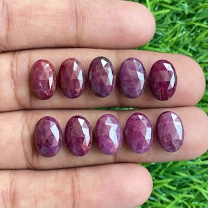 Pode incluir: Dez pedras preciosas de rubi de forma oval facetadas em vários tons de vermelho e roxo. As pedras preciosas estão dispostas em duas filas de cinco.