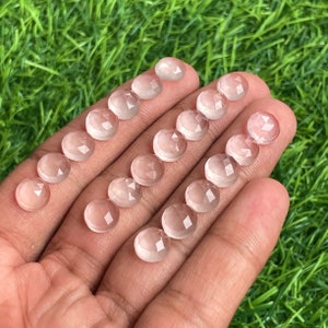 Könnte beinhalten: Eine Sammlung von 18 klaren, facettierten, runden Edelsteinkabochons. Die Cabochons sind in Reihen auf einer Hand angeordnet, wobei der größte Cabochon oben und der kleinste unten liegt.