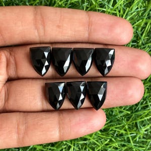 May include: Seven black faceted gemstone cabochons in a teardrop shape. The gemstones are arranged in two rows, with three in the top row and four in the bottom row.