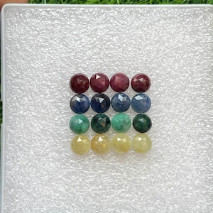 May include: A collection of 12 faceted gemstones in various colours, including red, blue, green, and yellow. The gemstones are arranged in four rows of three, with each row featuring a different colour.