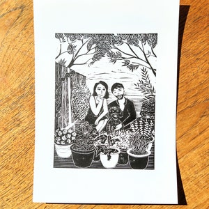 A black linocut portrait. A man and woman sit with their dog amongst plantpots.