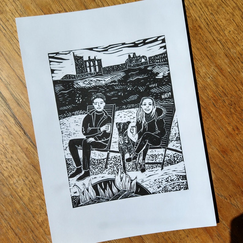 A black linocut portrait of a couple sitting on deck chairs on a beach. Between them is a greyhound and behind them is Tynemouth Abbey
