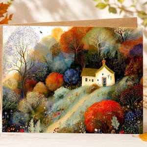 May include: A rectangular greeting card featuring a colorful illustration of a small cottage nestled in a dense forest during autumn. The scene displays vibrant orange, red, blue, and green trees, a winding path, and a light-colored house with a chimney.