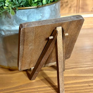May include: A small wooden easel with a brown finish. The easel has a rectangular frame and a simple design.