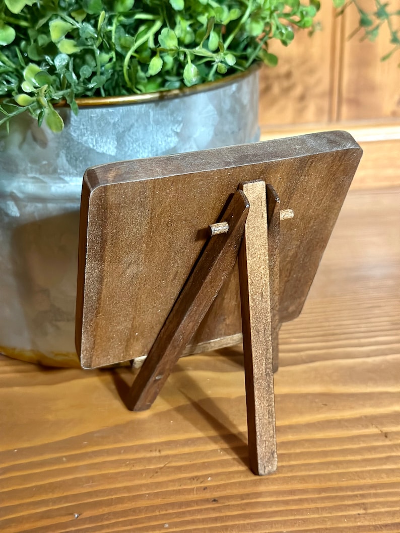 May include: A small wooden easel with a brown finish. The easel has a rectangular frame and a simple design.