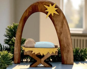 May include: Wooden nativity scene featuring a baby in a manger under an arch with a yellow star. The manger is yellow, and the baby is light blue and tan. The arch and manger frame are brown.