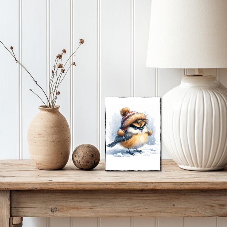 May include: A cartoon illustration of a small bird wearing a red and white knit hat with a pom pom on top. The bird is standing on a snowy surface with a grumpy expression.