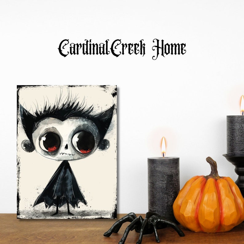 May include: A rectangular wall art print featuring a stylized illustration of a vampire character with large black eyes, red irises, and a black cape. The text Cardinal Creek Home is printed above the artwork in a black gothic-style font.
