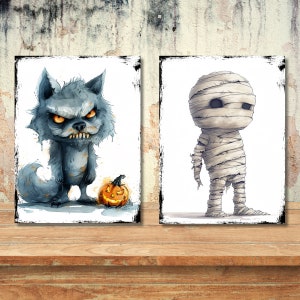 May include: Two rectangular wall art prints featuring Halloween characters. The left print shows a grey, furry werewolf with glowing orange eyes standing next to a carved jack-o'-lantern. The right print depicts a wrapped mummy figure.
