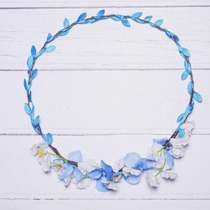 May include: A blue floral wreath with white flowers on a white wooden background.