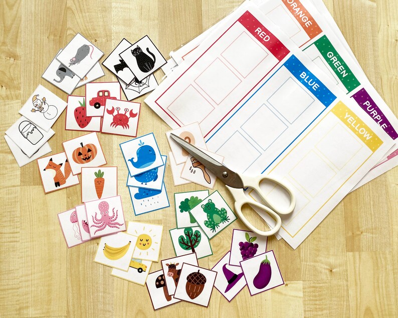 May include: A collection of colorful educational materials for children, including illustrated cards and color sorting sheets. The cards feature various objects and animals, while the sheets are labeled with colors like red, blue, and green. A pair of scissors is also present.