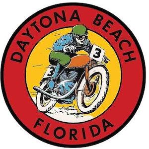 May include: A red, white and black circular sticker with the text "DAYTONA BEACH FLORIDA" and a cartoon image of a motorcyclist wearing a helmet and goggles, riding a motorbike with the number "3" on it.