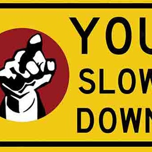 以下が含まれることがあります： 黒い縁取りのある黄色の警告標識で、「YOU SLOW DOWN」という文字が書かれています。標識の左上隅には、右を指す黒い手の赤い円があります。