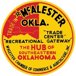 May include: A yellow and red circular logo with the text "TRADE IN MCALESTER OKLA." and "THE HUB OF SOUTHEASTERN OKLAHOMA" in black lettering. The logo also includes the text "TRADE CENTER" and "RECREATIONAL GATEWAY" in black lettering. The logo is surrounded by the text "MCALESTER CHAMBER OF COMMERCE & AGRICULTURE, INC."