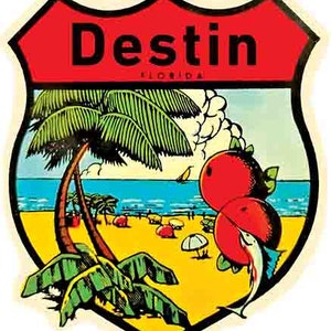 May include: A red and white shield-shaped sticker with the text "Destin Florida" in black lettering. The sticker features a palm tree, a beach scene, and two red fruits with a blue fish.