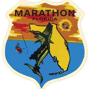 Op de afbeelding: Een vintage sticker in de vorm van een schild met een zonsondergangscène en een marlijn die uit het water springt. De sticker heeft de tekst "Marathon, Florida" en toont een cartoonzon met een zonnebril.