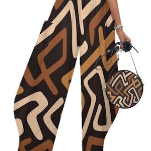 May include: Wide-leg pants with a geometric pattern in shades of brown, tan, and cream. The pants have pockets and are paired with a matching round handbag. The outfit is a stylish ensemble.