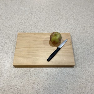 May include: A wooden cutting board with a green apple and a small silver knife with a black handle.