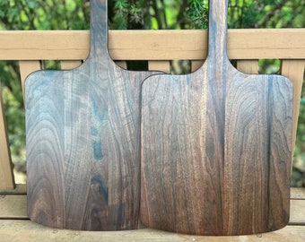 May include: Two dark brown wooden pizza peels with long handles. The peels are made of walnut wood and have a smooth, polished finish.
