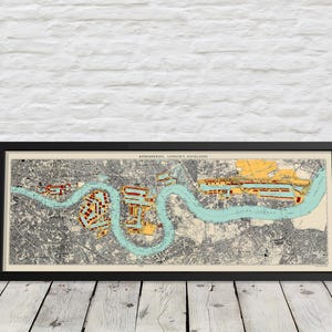 Peut inclure: Carte vintage encadrée des Docklands de Londres, avec une vue détaillée de la Tamise et des environs. La carte présente une rivière turquoise, des terres beiges et des rehauts rouges et jaunes. Le cadre est noir, et le texte "REMEMBERING LONDON'S DOCKLANDS" est visible.