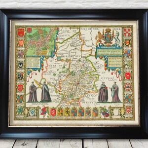 Op de afbeelding: Een antieke kaart van het eiland Ely, Engeland, met omliggende graafschappen, met wapenschilden en tekst. De kaart is ingelijst in een zwart frame.