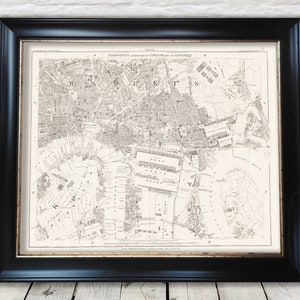 May include: A vintage black and white map of London and its suburbs, printed on paper and framed in a black frame. The map shows the city's streets, landmarks, and waterways. The title of the map is "STANFORD'S  CORRECTED MAP of LONDON and the SUBURBS."