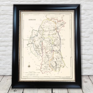 Może przedstawiać: Oprawiona mapa Armagh, Irlandia, w czarnej ramie. Mapa zawiera szczegółowe linie i tekst, z paletą kolorów beżu, zieleni, żółci i czerwieni. Słowo "Armagh" jest wydrukowane u góry mapy.