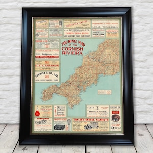 May include: Framed vintage map of the Cornish Riviera with a black frame. The map features a detailed road network and advertisements. The title "Touring Map of the Cornish Riviera" is prominently displayed. The map is set against a light blue background.