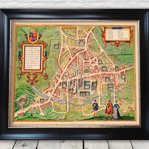 May include: Framed vintage map of Canterbury, England, featuring detailed city layout with buildings, streets, and a river. The map is in a black frame, with a colorful, aged appearance, and includes decorative text and figures.