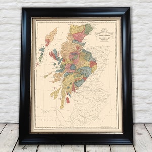 Op de afbeelding: Een vintage kaart van de Hooglanden en Graafschappen van Schotland, die de verschillende regio's in verschillende kleuren laat zien. De kaart is zwart ingelijst en heeft een witte achtergrond.