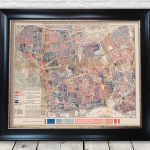 Op de afbeelding: Een ingelijste vintage kaart van de armoede in East End, samengesteld uit rapporten van schoolbestuursbezoekers in 1887. De kaart zit in een zwart frame en toont een gedetailleerde, kleurrijke weergave van het gebied.