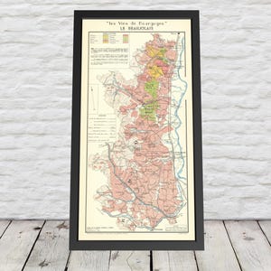 May include: Framed vintage map print of the Beaujolais wine region in France. The map features detailed illustrations in shades of pink, green, yellow, and beige, with text in French. The map is encased in a black frame.