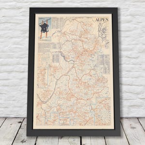 May include: Framed vintage map print of the Alps region, with detailed cartography in red and blue lines on a cream background. The map is in a black frame, leaning against a white brick wall and wooden floor.