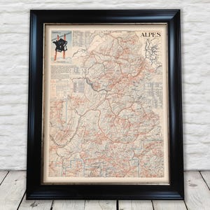 May include: A framed vintage map of the Alps region in France, featuring detailed topographical lines, geographical labels, and a small inset graphic in the top left corner showing a skier silhouette with the text CARTE DES SPORTS D'HIVER FRANCE.