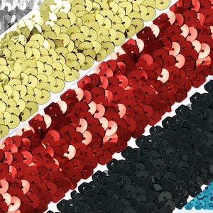 May include: A close-up of five different colors of sequin trim. The trim is made of small, round sequins that are sewn together in a continuous line. The colors are silver, gold, red, black, and blue.