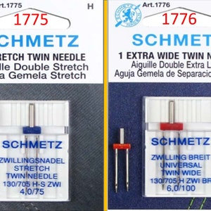 May include: Two packages of Schmetz sewing machine needles. One package is labeled "1 Stretch Twin Needle" and the other is labeled "1 Extra Wide Twin Needle". Each package contains needles with blue or red tops, and the text "Schmetz" is visible.
