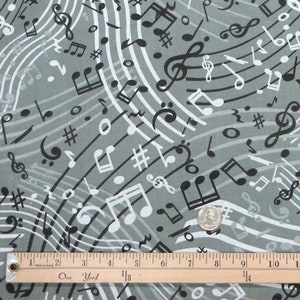 May include: Gray fabric with a repeating pattern of black and white musical notes and treble clefs. The fabric is measured with a ruler that reads "One Yard".