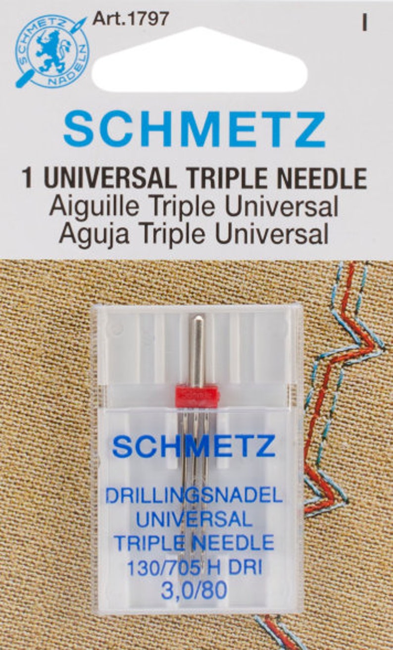 May include: A clear plastic package containing a SCHMETZ Universal Triple Needle. The package has blue and white text, including "SCHMETZ" and "1 UNIVERSAL TRIPLE NEEDLE." The needles are silver with a red plastic base. The package also includes the text "130/705 H DRI 3,0/80."