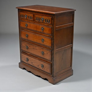 May include: A tall, wooden chest of drawers. It has six drawers and a rectangular top. The chest is made of dark brown wood with ornate metal handles. The drawers have a curved bottom edge.