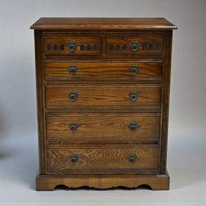 May include: A six-drawer oak chest with decorative metal handles. The chest has a warm, brown finish and is approximately 100 cm tall. The top two drawers feature decorative carvings. A classic piece of furniture.