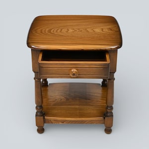 May include: A wooden side table in a warm brown finish. It has a rectangular top with rounded edges, a single drawer with a round knob, and a lower shelf. The table has four sturdy legs and is designed for storage and display.