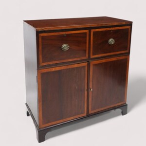 May include: A mahogany wood cabinet with two drawers and two doors. The cabinet has brass hardware and a dark wood finish.